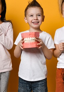 Three kids holding oversized toothbrushes and model teeth smiling with goldenrod background