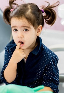 Little girl with pigtails in blue polka dot shirt touching her teeth with sad expression