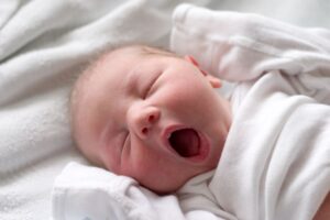 Cute yawning baby dressed in white onesie